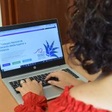 Mujer frente a la computadora con página del coloquio