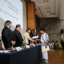 Egresado de bachillerato recibiendo sus documentos de manos de la Rectora María Esther Avelar